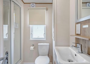 Ein Badezimmer mit Toilette, Dusche, Waschbecken, einem Fenster mit Jalousie und einem Spiegel.