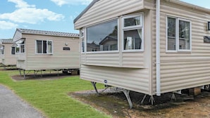 A row of mobile homes with a flat roof, a window, and a door, all elevated on stilts. - Bronze 2 Bedroom Caravan, Sleeps 6. With parking (Great Yarmouth)