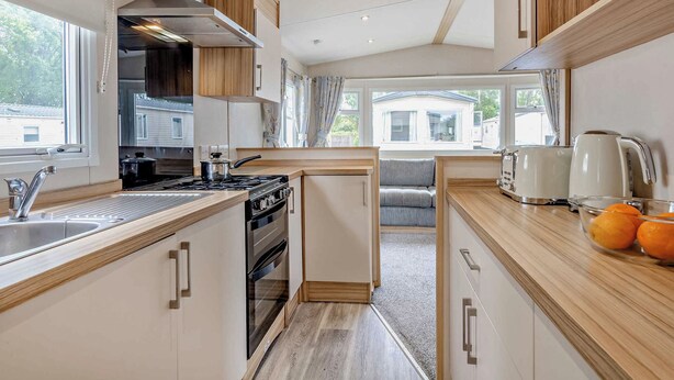 A modern kitchen with a stove, sink, and a view of the outside. - Bronze 2 Bedroom Caravan, Sleeps 6. With parking (Great Yarmouth)