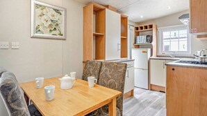 Een compacte keuken met houten kastjes, een eettafel met vier witte mokken, een gestreept stoel en een magnetron op het aanrecht.