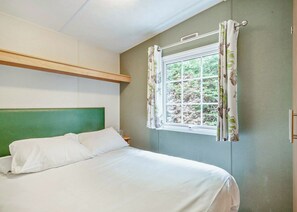 Ein Schlafzimmer mit einem grünen Kopfteil, einem Fenster mit blumigen Vorhängen und Blick ins Grüne.