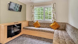 Een kamer met een bank, een televisie, een raam met gordijnen en een vloerbedekking.