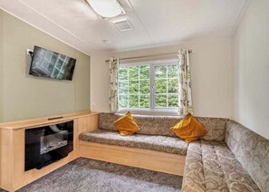 Ein Zimmer mit einer Couch, einem Fernseher, einem Fenster mit Vorhängen und einem Teppichboden.