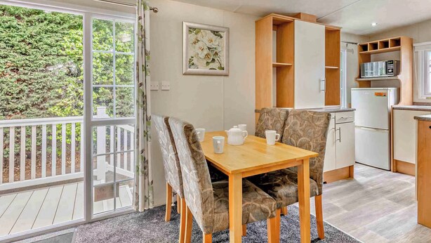 Een eethoek met een tafel en stoelen, een keuken met kasten en apparatuur, en een schuifdeur naar een balkon.