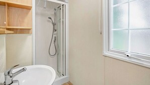 Een badkamer met douche, wastafel, raam en houten planken.