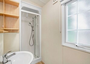 Ein Badezimmer mit Dusche, Waschbecken, einem Fenster und Holzregalen.