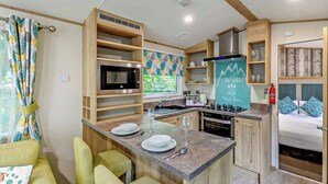 A compact kitchen with a microwave, stove, and sink, wooden cabinets, and a chalkboard with a motivational quote. - Bronze Premium 1 Bedroom Caravan, Sleeps 2 (Great Yarmouth)