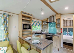 A compact kitchen with a microwave, stove, and sink, wooden cabinets, and a chalkboard with a motivational quote. - Bronze Premium 1 Bedroom Caravan, Sleeps 2 (Great Yarmouth)