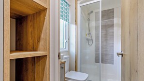 A bathroom with a shower, toilet, and wooden shelving. - Bronze Premium 1 Bedroom Caravan, Sleeps 2 (Great Yarmouth)