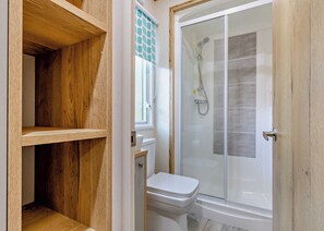 A bathroom with a shower, toilet, and wooden shelving. - Bronze Premium 1 Bedroom Caravan, Sleeps 2 (Great Yarmouth)