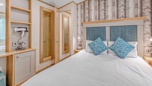 A bedroom with a bed, two nightstands, a mirror, and a built-in hairdryer. - Bronze Premium 1 Bedroom Caravan, Sleeps 2 (Great Yarmouth)