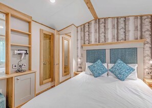 A bedroom with a bed, two nightstands, a mirror, and a built-in hairdryer. - Bronze Premium 1 Bedroom Caravan, Sleeps 2 (Great Yarmouth)