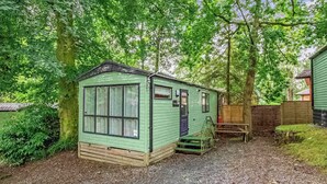 A small, single-story, green mobile home with a front porch, a window, and a door. - Bronze Premium 1 Bedroom Caravan, Sleeps 2 (Great Yarmouth)