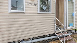 Un'abitazione mobile con una porta scorrevole, una finestra e un piccolo spazio esterno con delle gradinate.