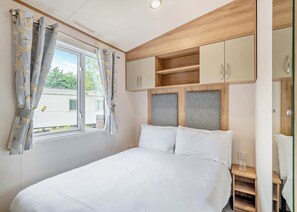 Ein Schlafzimmer mit Bett, einem Vorhangfenster, einem Holz-Kopfteil und eingebauten Schränken.