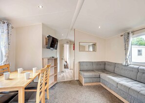 A room with a dining table, chairs, a sofa, a television, and a mirror. - Gold 4 Bedroom Caravan, Sleeps 10. With parking (Great Yarmouth)