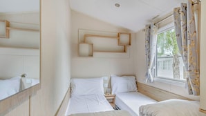 Una camera da letto con due letti, uno specchio, una finestra con tende e un poggiatesta con motivo geometrico.