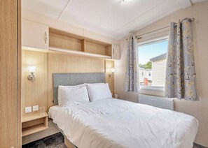 Ein Schlafzimmer mit Bett, Nachttischlampen, einem Fenster mit Vorhängen und eingebauten Regalen.