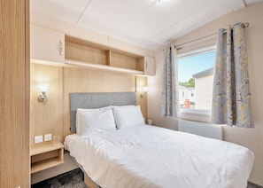Ein Schlafzimmer mit Bett, Nachttischlampen, einem Fenster mit Vorhängen und einem eingebauten Regal.