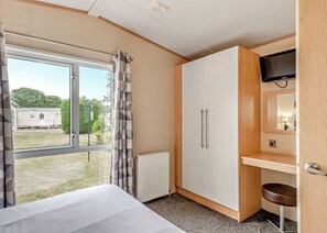 A room with a bed, a wardrobe, a desk with a chair, a radiator, and a TV. - Silver Caravan with ensuite (Great Yarmouth)