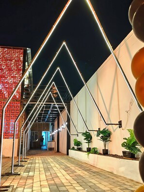 A pathway lined with geometric light installations, potted plants, and a red lattice structure. - Hotel Bobby Beach House (Puri)