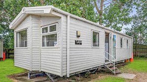A mobile home with a front porch, a small attached garage, and a water line running along the side. - Silver 3 Bedroom Caravan, Sleeps 8 (Great Yarmouth)