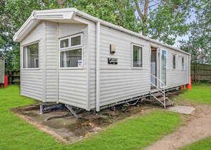 Une maison mobile dotée d’un porche à l’avant, d’un petit garage attenant et d’une conduite d’eau qui longe le côté.