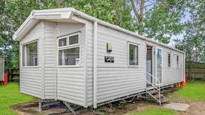 A mobile home with a front porch, a small attached garage, and a visible water line. - Silver Caravan with parking (Great Yarmouth)