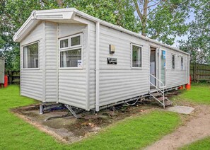 A mobile home with a front porch, a small attached garage, and a visible water line. - Silver Caravan with parking (Great Yarmouth)