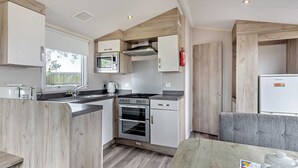 A compact kitchen with a microwave, stove, oven, and a small refrigerator. - Silver Caravan with parking (Great Yarmouth)