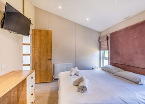 Une chambre à coucher avec un lit, une armoire en bois, une télévision, un radiateur et une fenêtre avec des rideaux.