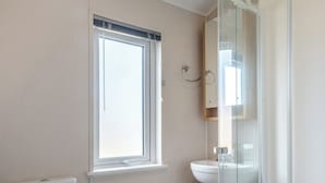 Et badeværelse med et vindue, toilet og en brusekabine i glas.
