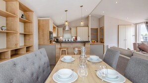 Una cocina moderna con armarios de madera, una isla central y un comedor con sillas tapizadas en gris y una mesa de madera dispuesta para cuatro.