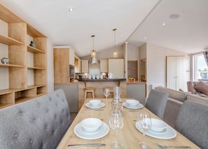 A modern kitchen with wooden cabinets, a central island, and a dining area with grey upholstered chairs and a wooden table set for four.