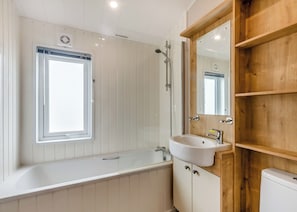 A bathroom with a window, a bathtub, a sink, and a wooden shelf.