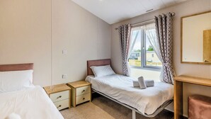 Un dormitorio con una cama individual, una mesita de noche y un banco de madera. Cuenta también con cortinas y una ventana.