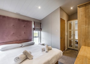A bedroom with a large bed, a wooden wardrobe, and a window with a view.
