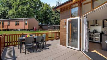 A covered outdoor patio with a table and chairs, a sliding glass door leading to a kitchen, and a wooden deck.