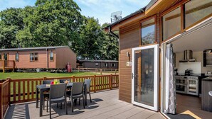 Un patio techado al aire libre con una mesa y sillas, una puerta corrediza de vidrio que da a una cocina y una terraza de madera.