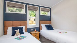 A bedroom with two beds, a window, and a nightstand with a lamp. - Deluxe 4, Slps 8, parking, ensuite, decking (Near Weymouth)