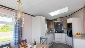 A modern kitchen with white cabinets, a built-in oven, and a dining area with a wooden table and chairs. - Deluxe 4, Slps 8, parking, ensuite, decking (Near Weymouth)