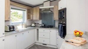 A modern kitchen with white cabinets, a gas stove, a microwave, and a window providing natural light. - Deluxe 4, Slps 8, parking, ensuite, decking (Near Weymouth)