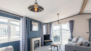 A living room with a fireplace, sofa, television, and a balcony view. - Deluxe 4, Slps 8, parking, ensuite, decking (Near Weymouth)