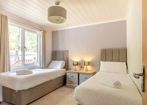 A double room with two beds, a window with curtains, a bedside table with lamps, and a ceiling light. - Prestige 3, Slps 6, parking, ensuite, deck, LV HT (Near Weymouth)