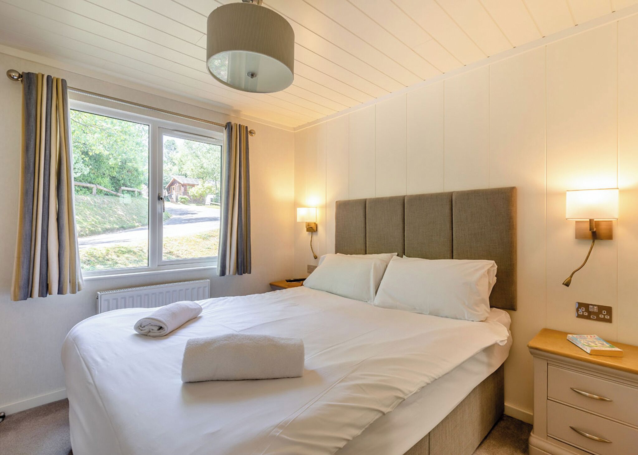A hotel room with a large bed, a window with curtains, a bedside lamp, and a nightstand.