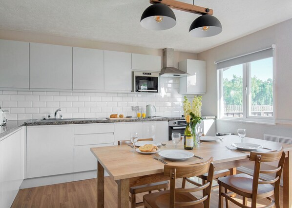 A modern kitchen with white cabinetry, a wooden dining table, and two pendant lights.