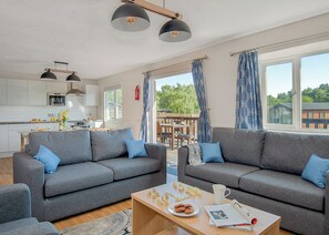 A modern living room with grey sofas, a wooden coffee table, and a view of an outdoor deck.