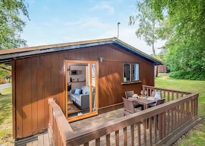 A compact wooden cabin with a deck, a kitchenette, and a seating area with a table and chairs.
