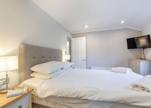 A hotel room with a bed, a nightstand, a lamp, a TV, and a dresser.
