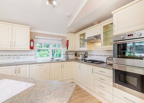 Una cocina moderna con armarios blancos, una estufa a gas, un horno y un ventanal con vistas al verdor.